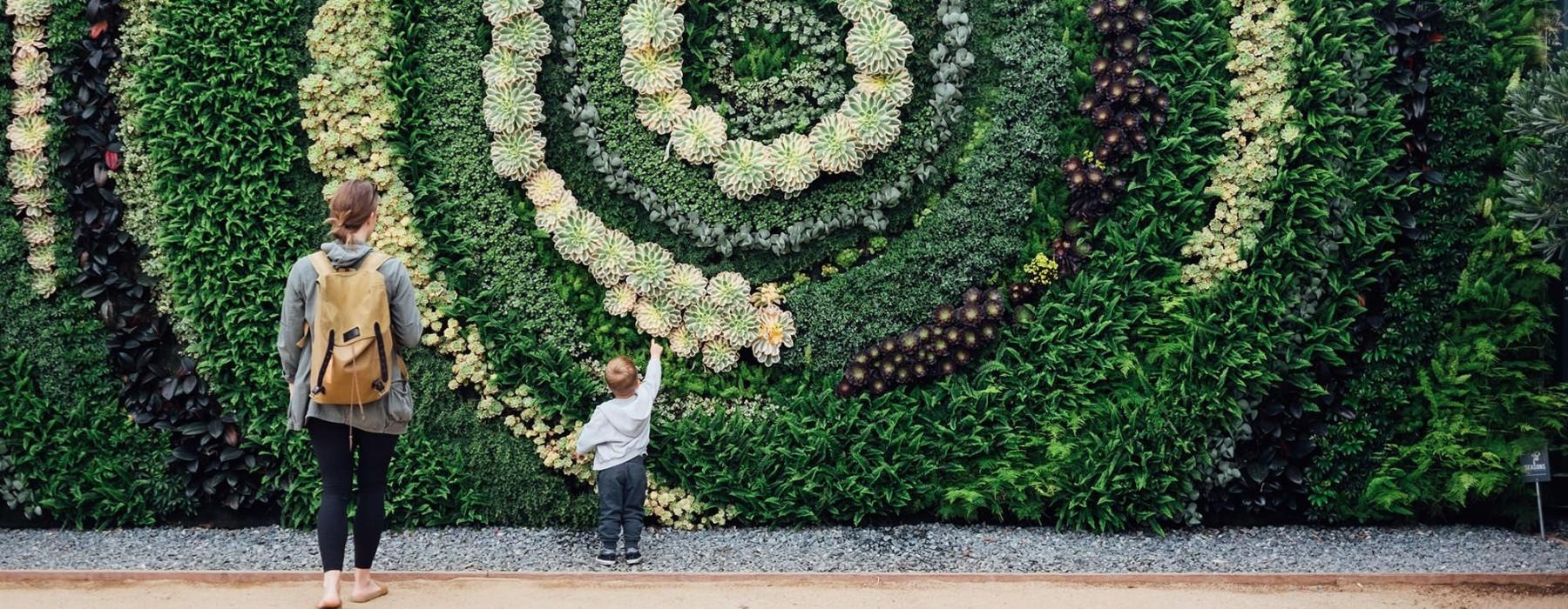 mother and child standing in front of a mural made of plants